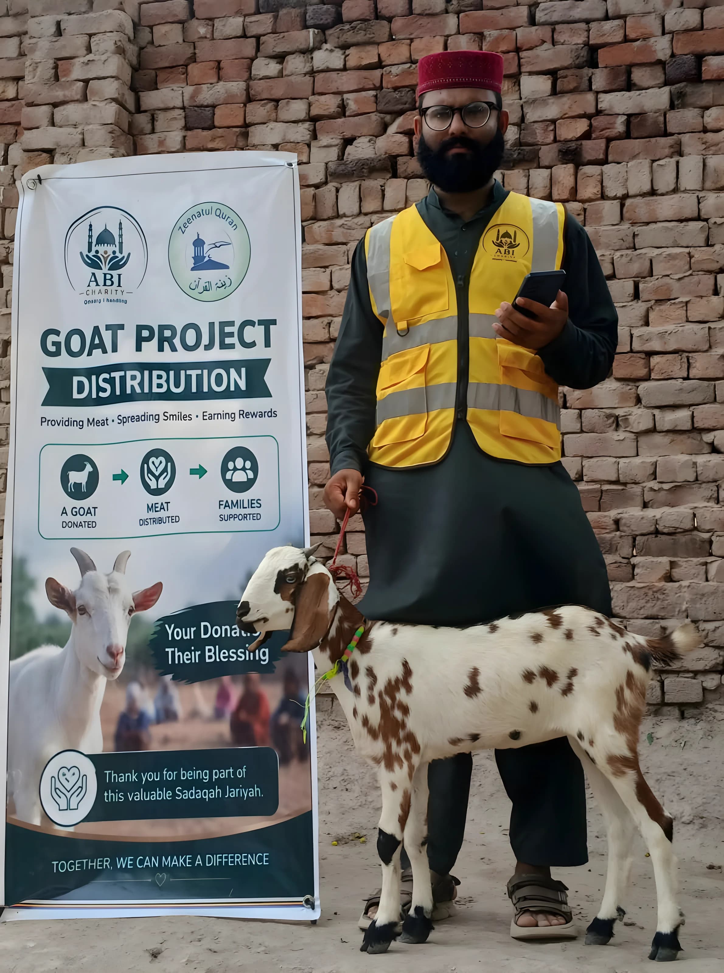 Mann i ABI Charitys vest holder en brunflekket geit i tau, ved et banner med ABI Charitys logo og teksten «Goat Project Distribution»