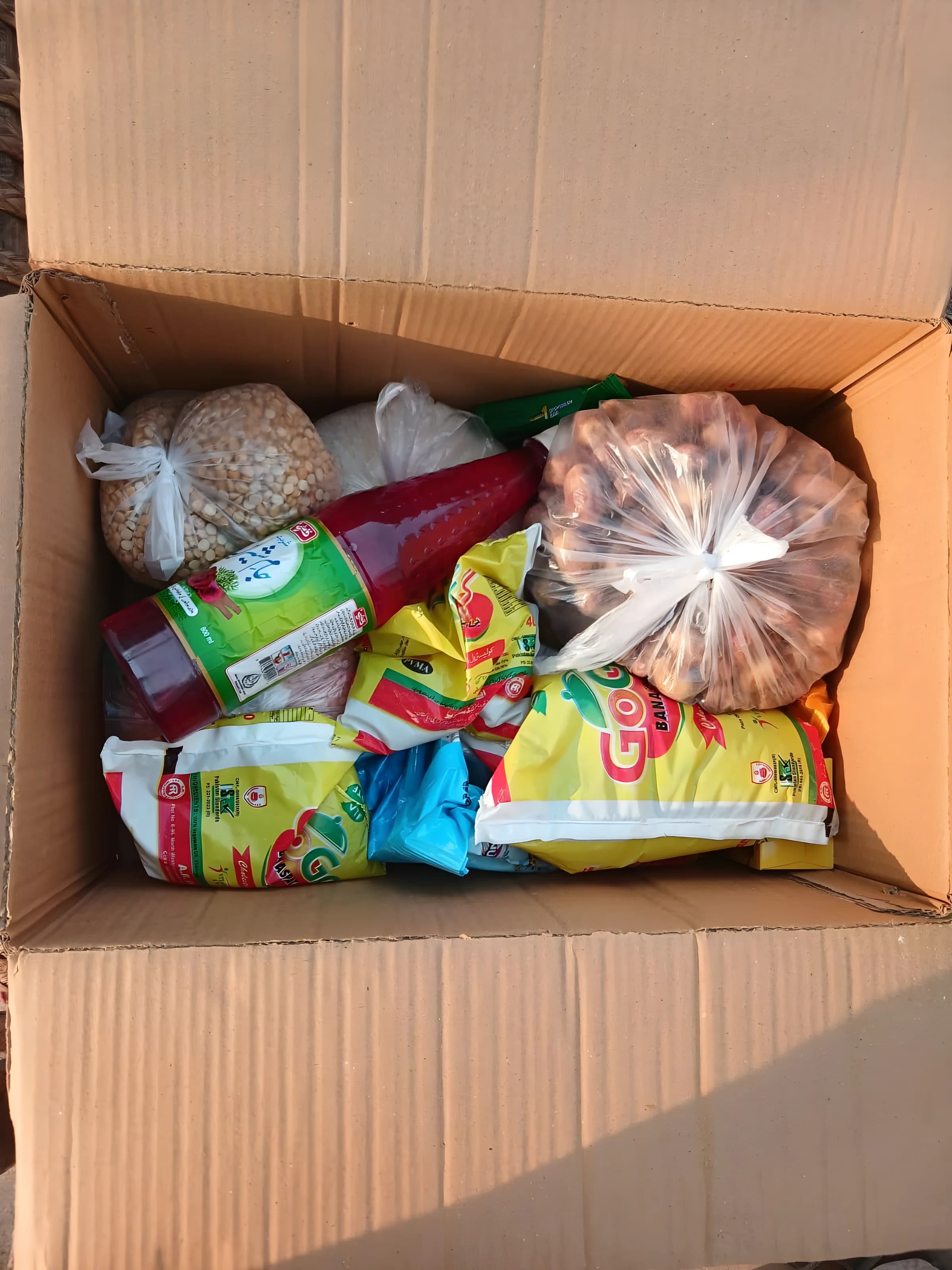 Åpen pappeske sett ovenfra, med linser, dadler, ris, saft, matolje og te